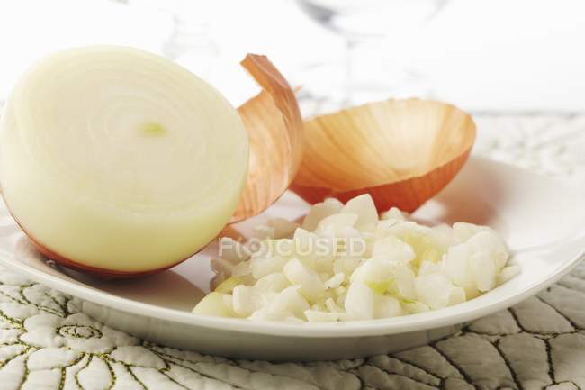 Oignon blanc haché avec un demi-oignon ; peau d'oignon sur plaque blanche — Photo de stock