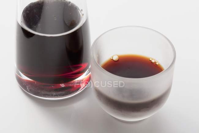 Molho de soja em uma garrafa e em um copo em uma superfície branca — Fotografia de Stock