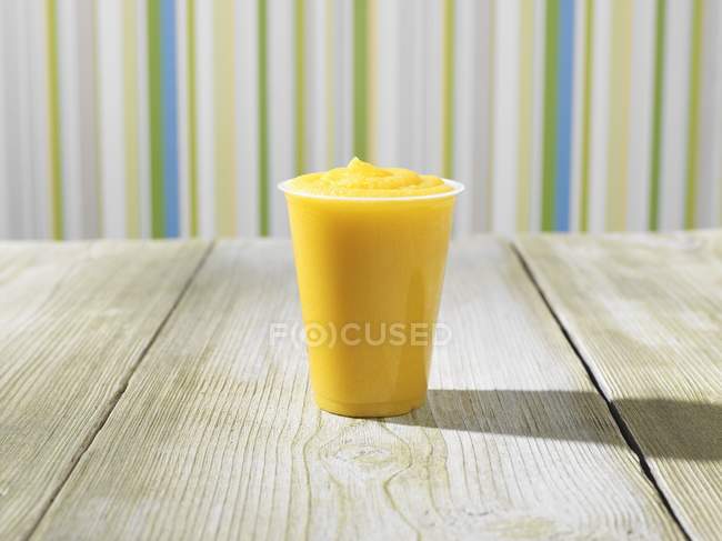 Closeup view of fruit Frappe in plastic cup on wooden surface — Stock Photo