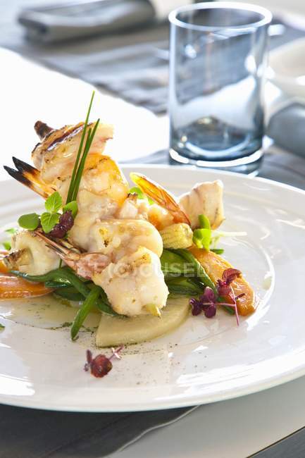 Crevettes et brochettes de poisson moine sur un lit de légumes sur assiette blanche — Photo de stock