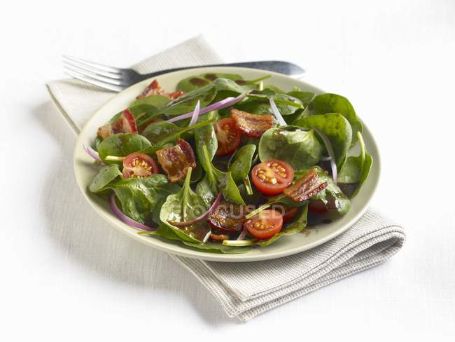 Salada de espinafre com bacon e tomate cereja em prato branco sobre toalha — Fotografia de Stock