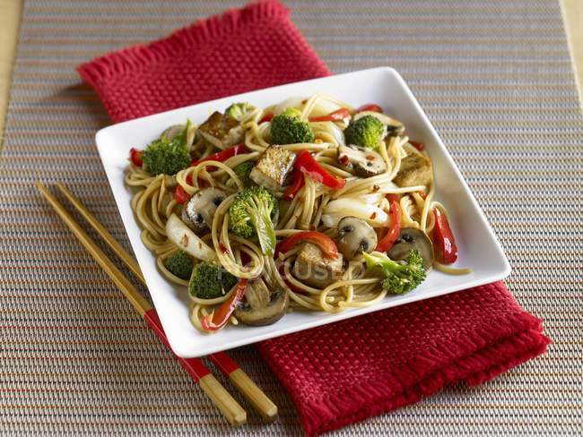 Tofu und Gemüse unter Rühren mit Nudeln auf weißem Teller auf rotem Handtuch anbraten — Stockfoto