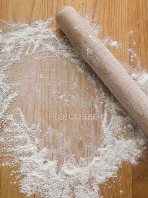 Vue surélevée de farine saupoudrée sur une surface en bois avec un rouleau à pâtisserie — Photo de stock