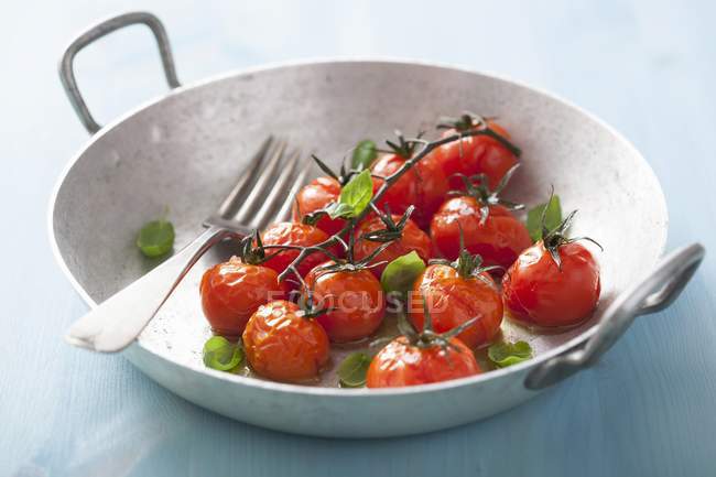 Roasted cherry tomatoes with basil in wok with fork — Stock Photo