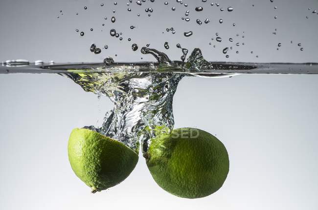 Limes falling into water — Stock Photo