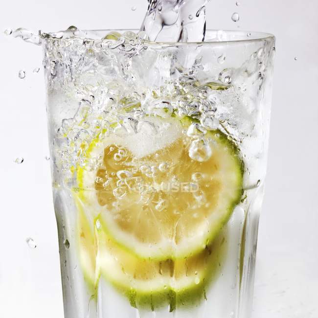 Vista close-up de derramar água para o vidro de fatias de limão — Fotografia de Stock