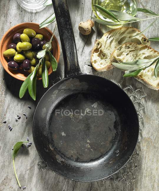 Пустая сковорода, шалфей, оливки, оливковое масло, оливковая веточка, оливковый чиабатта и лаванда — стоковое фото