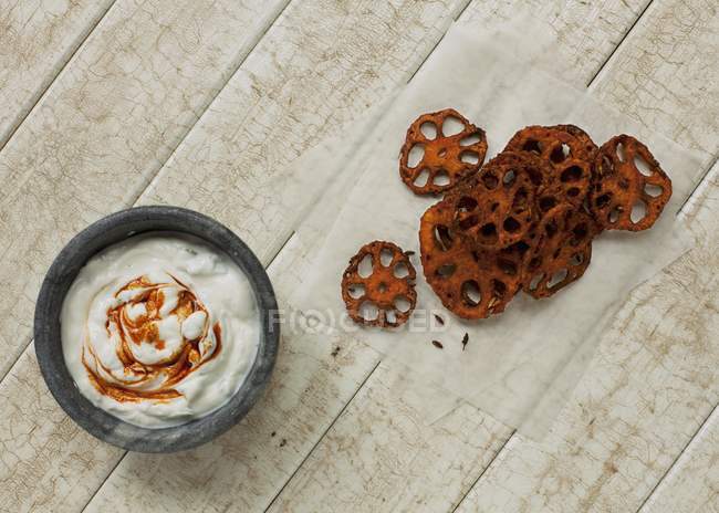Ein würziger Joghurt-Dip mit im Ofen gebackenen Lotuswurzel-Chips auf Holzgrund — Stockfoto