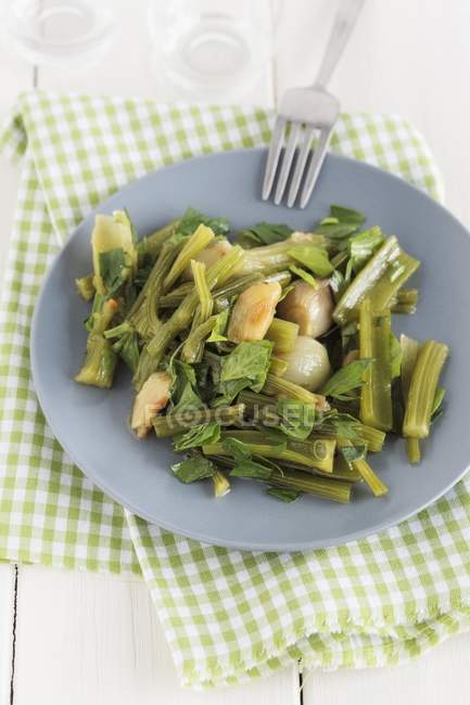 Cooked celery with onions on blue plate with fork — Stock Photo