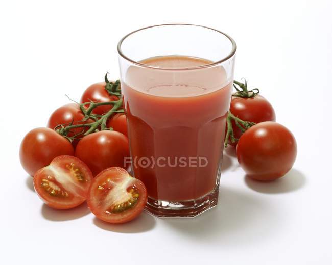 Verre de jus de tomate entouré de tomates — Photo de stock