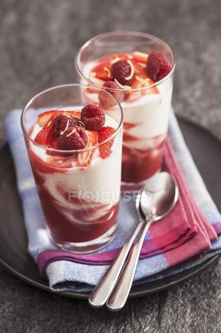 Vista de cerca de dos vasos de yogur con coulis de frutas, bayas rojas frescas y ralladura de limón - foto de stock