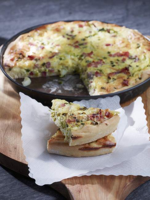 Quiche with potatoes, bacon and leek on wooden desk with dish and towel — Stock Photo