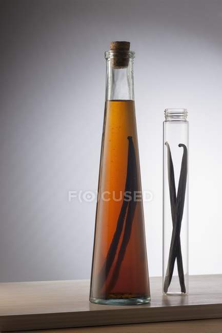 Una bottiglia di estratto di vaniglia e due baccelli di vaniglia in un tubo di vetro — Foto stock