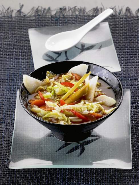 Pointed cabbage with vegetables and lemongrass in black bowl over white platter — Stock Photo