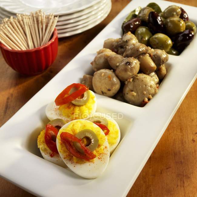 Три частини виступає блюдо з Deviled яйця, мариновані гриби та оливками; Чаша зубочистки на білий плита — стокове фото