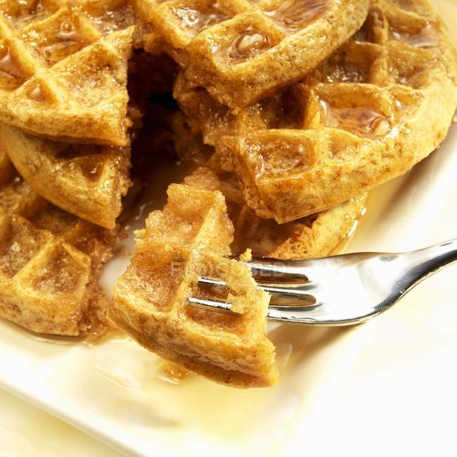 Vista close-up de waffles de grãos com xarope de bordo com peça em garfo — Fotografia de Stock