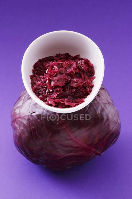Red cabbage in a bowl on top of a red cabbage on purple surface — Stock Photo