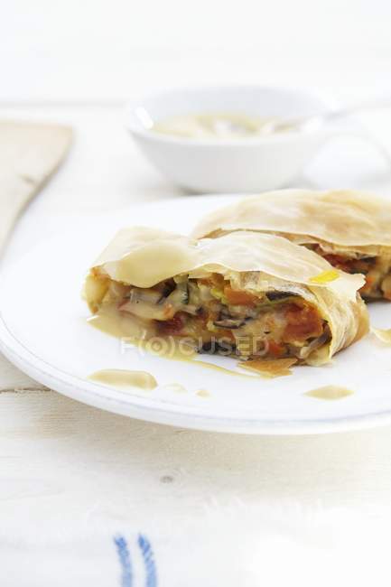 Vegetable strudel with sauce in white plate over cloth — Stock Photo
