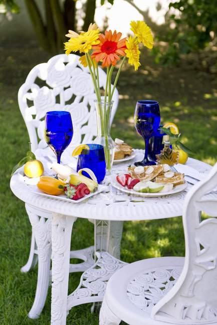Daytime view of outdoor table with Belgian waffle breakfast, flowers in vase — Stock Photo