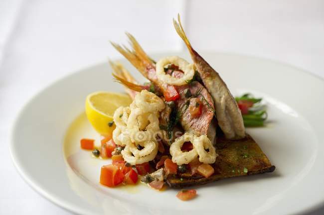 Closeup view of red snappers with fried calamari and lemon half on white plate — Stock Photo
