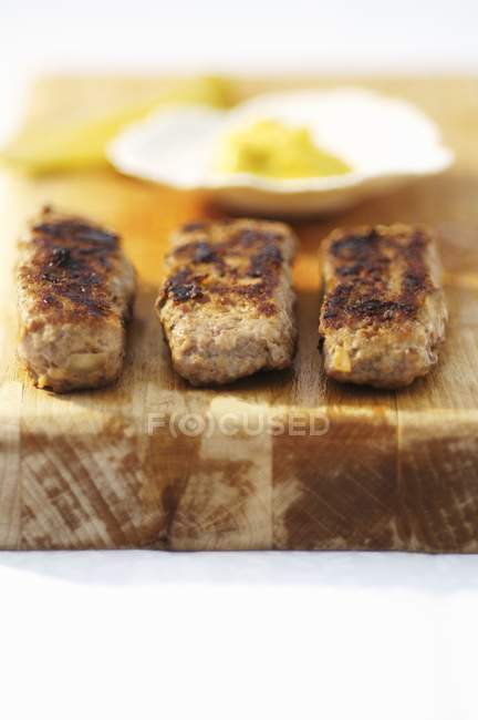 Closeup view of fried sausages with mustard on wooden board — Stock Photo
