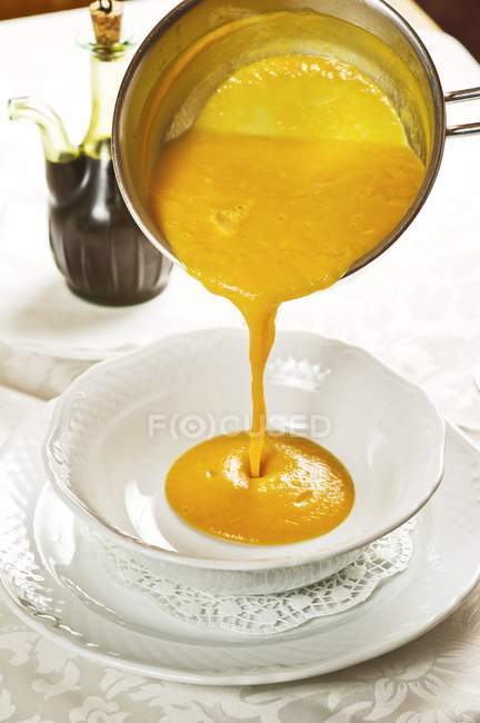 Pumpkin soup pouring into soup bowl — Stock Photo