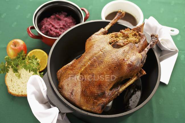 Stuffed goose with red cabbage in black pot over green surface — Stock Photo
