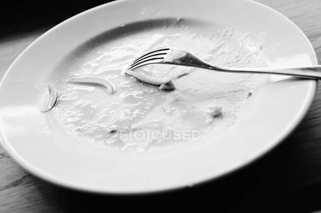 Closeup view of dirty white plate with vegetable and sauce leftovers and fork — Stock Photo
