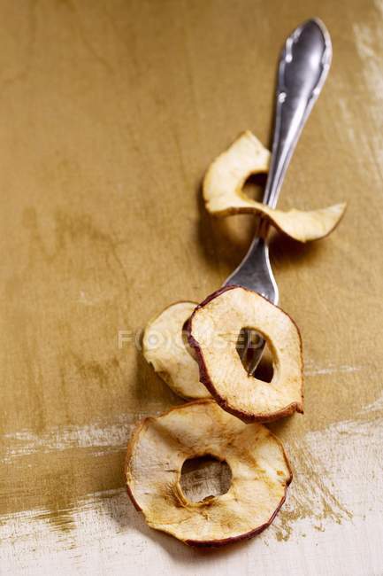 Vista de cerca de patatas fritas de manzana seca y tenedor en la superficie de madera - foto de stock