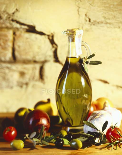 Una caraffa di olio d'oliva con olive e pomodori contro muro di mattoni — Foto stock