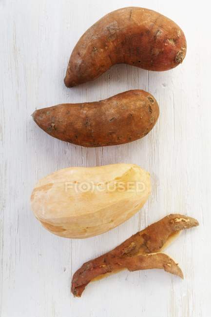 Batatas doces, descascadas e não descascadas na superfície de madeira — Fotografia de Stock