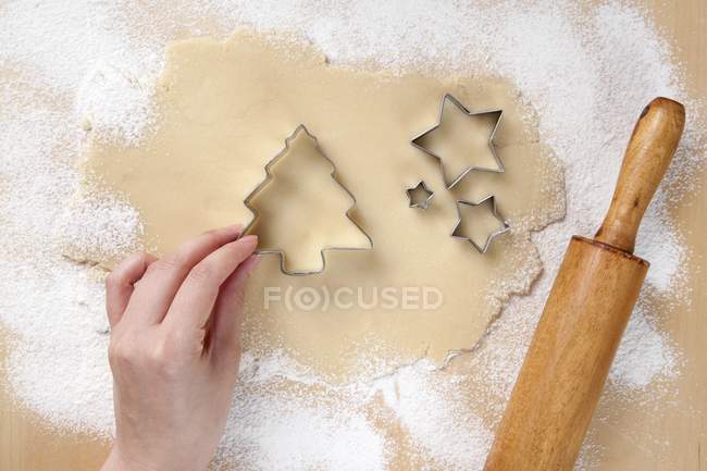 Vista dall'alto di mano posizionare albero di Natale tagliabiscotti su pasta rotolata da tagliabiscotti a forma di stella — Foto stock