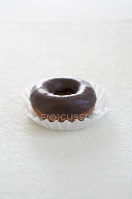 Vista de primer plano de la rosquilla vidriada de chocolate en la taza de papel y la superficie blanca - foto de stock