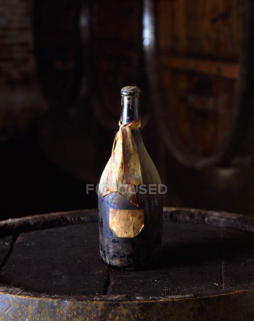 An antique wine bottle with labels on an old wooden barrel — Stock Photo