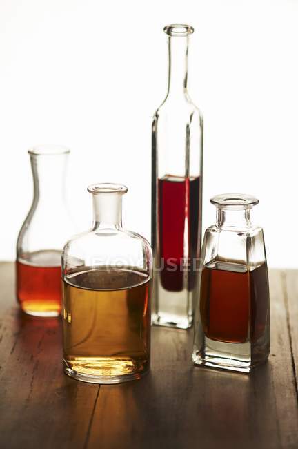 Vista de primer plano de cuatro botellas de vidrio surtidos de vinagres - foto de stock