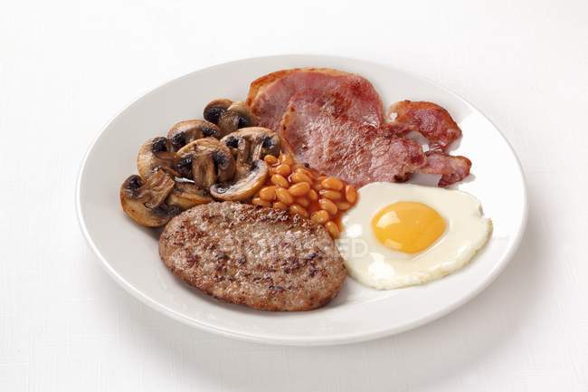 Vue rapprochée du petit déjeuner anglais avec haricots cuits au four, bacon et oeuf frit — Photo de stock