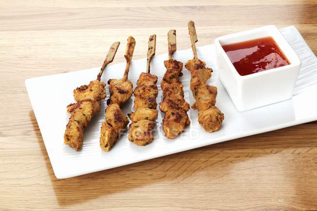 Chicken kebabs with barbecue sauce on platter on wood surface — Stock Photo