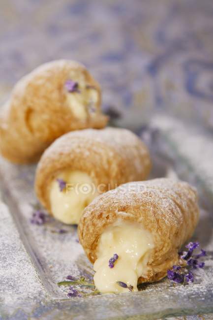 Closeup view of puff pastry rolls filled with cream and garnished with edible flowers — Stock Photo