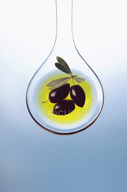 Оливковое масло и оливки на ложке салата — стоковое фото