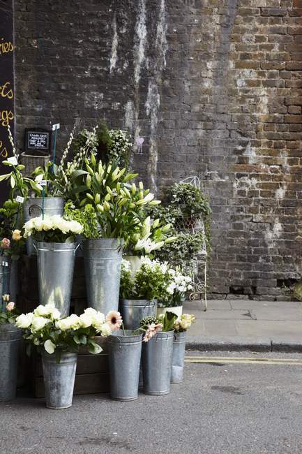 Дневной вид на цветочный киоск с цинковыми вазами перед старой кирпичной стеной — стоковое фото