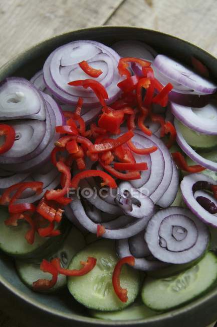 Onion rings, cucumber slices and chillis on black plate over wooden surface — Stock Photo