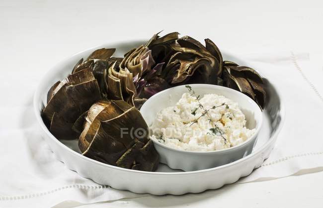 Carciofi con un tuffo di aglio su piatto bianco sopra asciugamano — Foto stock