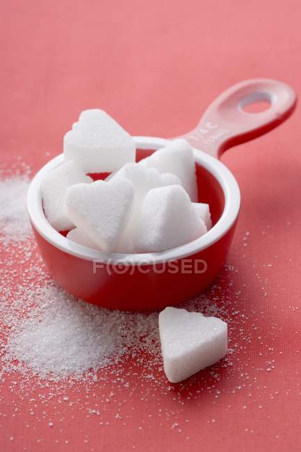 Closeup view of heart-shaped sugar lumps in red measuring cup — Stock Photo