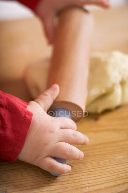Vue rapprochée des mains de l'enfant déroulant la pâte — Photo de stock