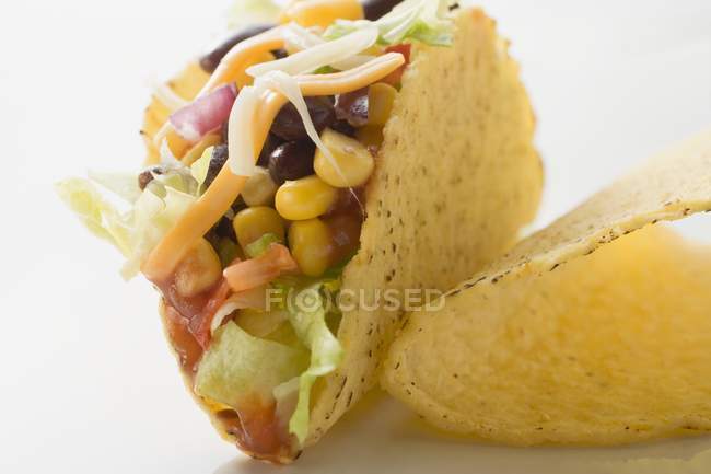 Taco relleno con maíz dulce y frijoles que ponen en la superficie blanca - foto de stock