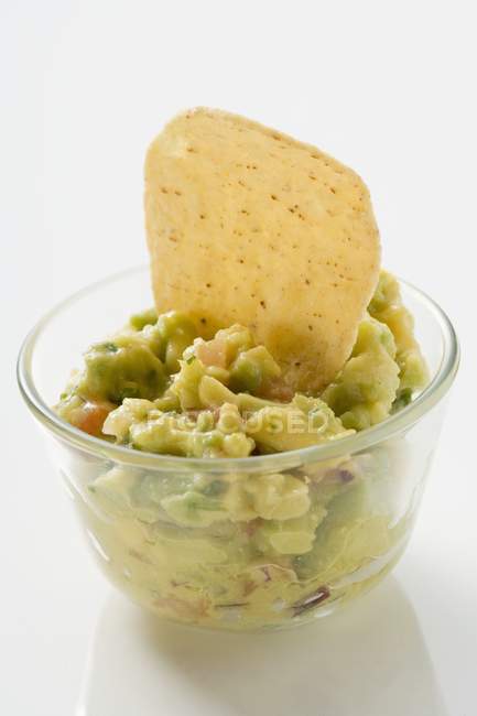 Guacamole com chip de tortilla em tigela de vidro pequeno sobre a superfície branca — Fotografia de Stock