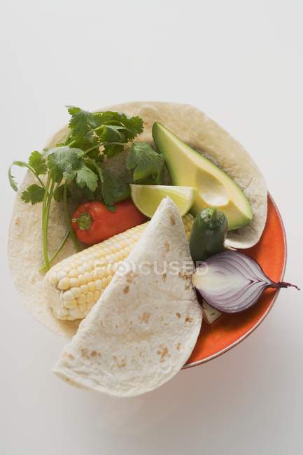 Top view of corn cob with avocado, peppers, herb, onion and lime in bowl — Stock Photo