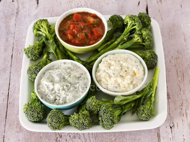 Broccoli and three different dips on white plate  over wooden surface — Stock Photo