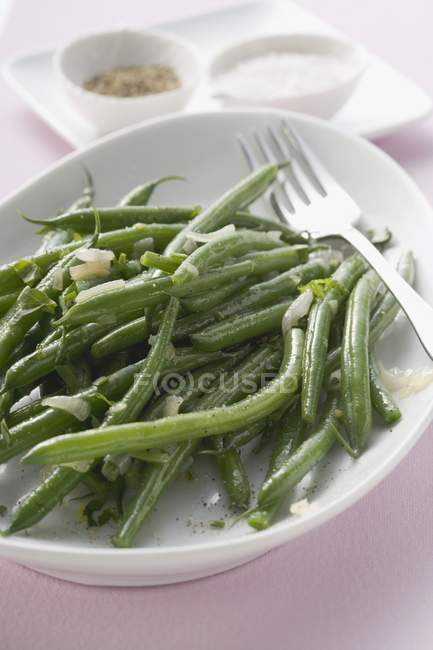 Grüne Bohnen mit Zwiebeln, Salz und Pfeffer im Hintergrund — Stockfoto