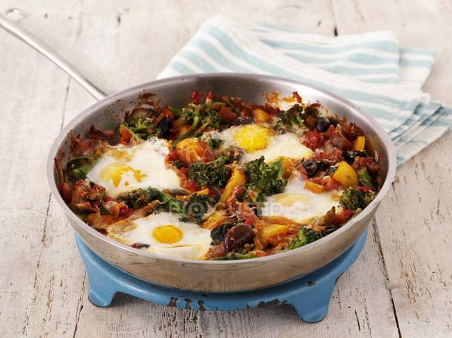 Fried eggs with broccoli and pepper in a pan on wooden surface — Stock Photo